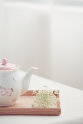 A minimalist ceramic teapot with soft steam rising, set on a wooden tray.