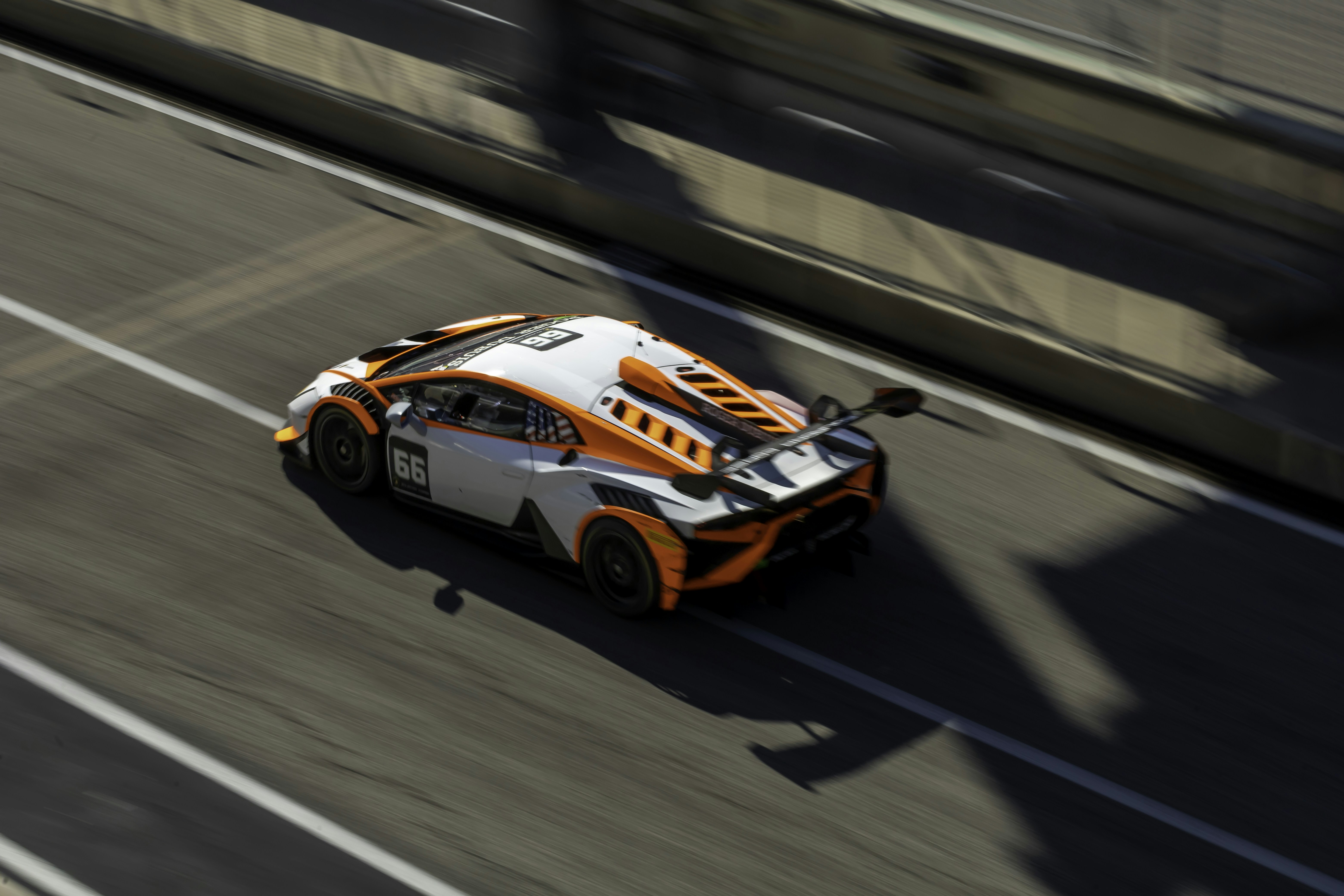 An orange and white race car driving down a road photo – Free Cota ...