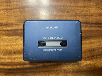 A vintage AIWA stereo cassette player with a blue casing featuring an 'AUTO REVERSE' function. The player rests on a wooden surface, showing signs of wear such as scratches.