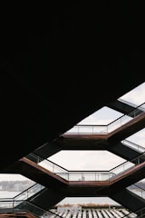 Geometric architecture with a view through several interconnected stairway platforms. The design features a series of horizontal lines and angles, framing a distant cityscape and a body of water in the background.