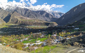 Wide shot of multiple chalets nestled in a lush green valley under a clear blue sky.