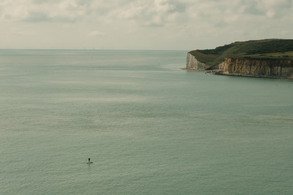 a lone person standing on a surfboard in the middle of the ocean