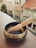 A Tibetan singing bowl with decorative patterns and a wooden mallet resting inside, positioned on a wooden ledge. In the background, several houses with light blue and beige walls and tiled roofs are visible, blurred out of focus.