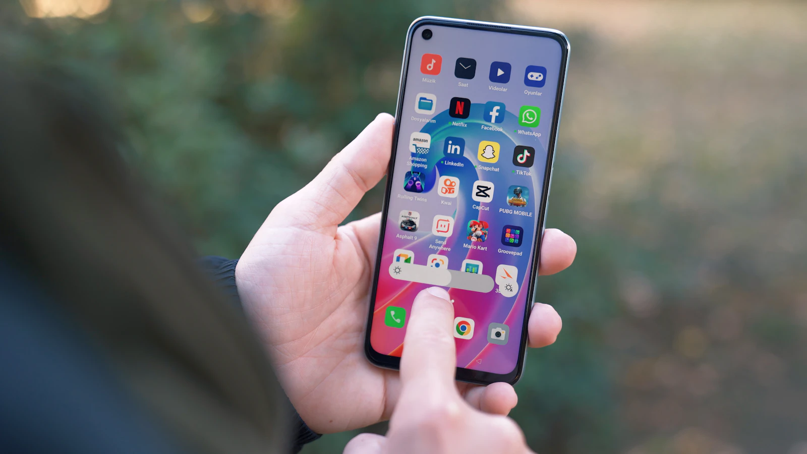 A hand holding an Android phone open on its home screen