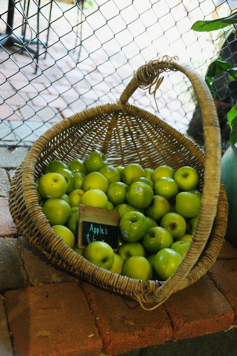 a basket full of green apples sitting on a brick floor