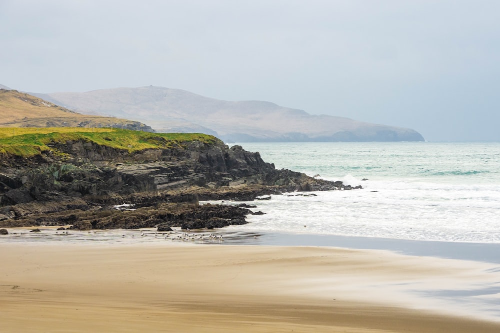 a sandy beach next to the ocean with mountains in the background