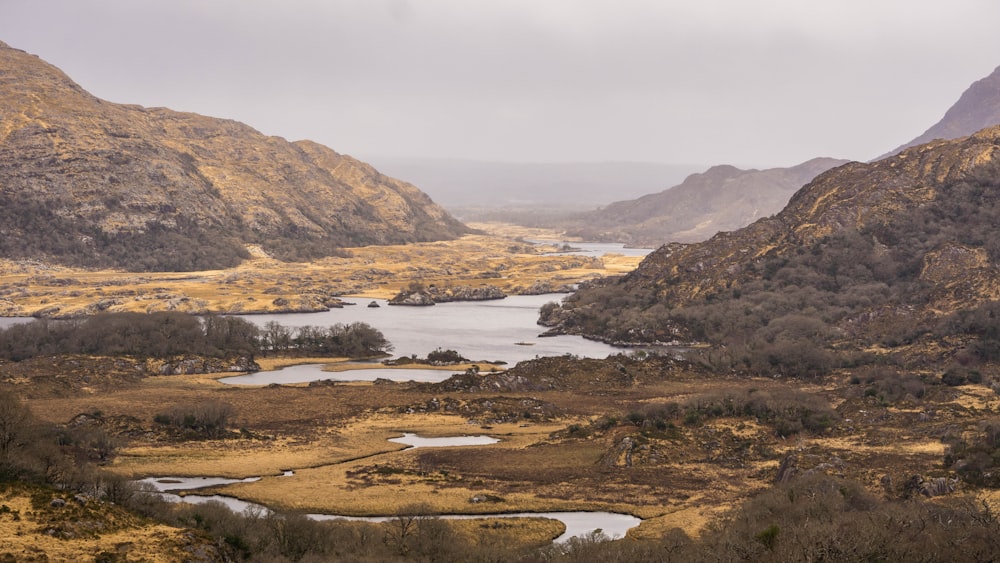 a view of a valley with a lake and mountains in the background