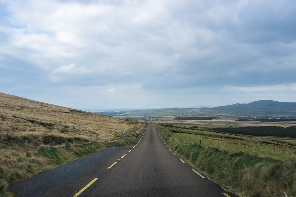 a long empty road with a grassy hill in the background