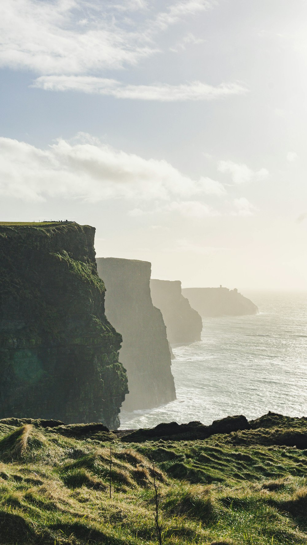 a grassy field next to a cliff overlooking the ocean