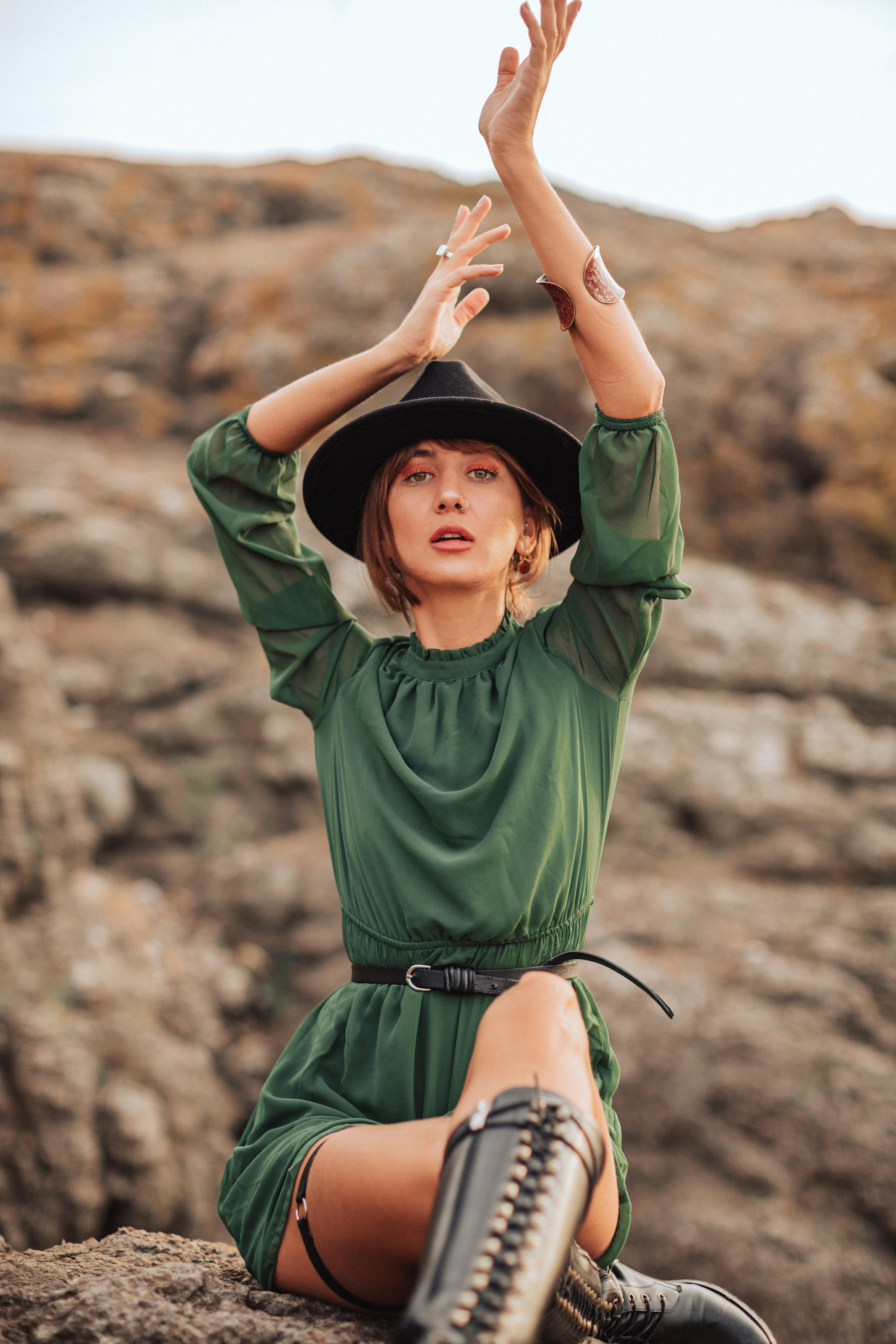 a woman in a green dress and hat sitting on a rock