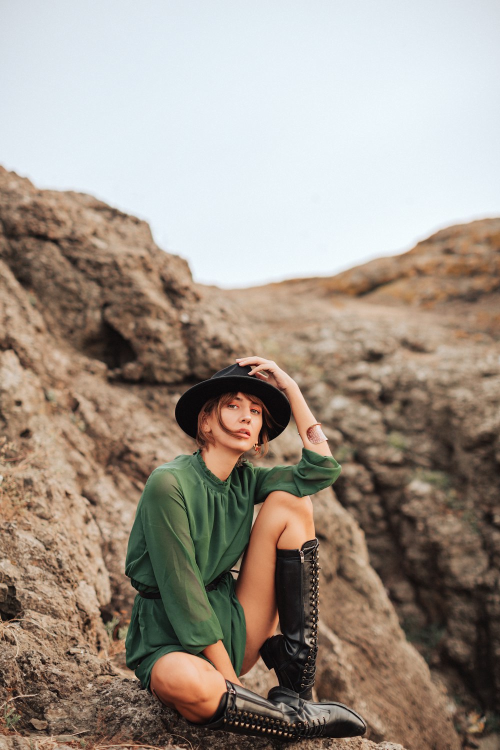 a woman sitting on a rock wearing a hat and boots