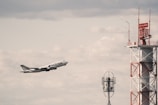 A large aircraft labeled 'NATIONAL' is taking off into a cloudy sky. The image also features a tall communication tower with red and white markings. Another smaller antenna is visible in the mid-ground.