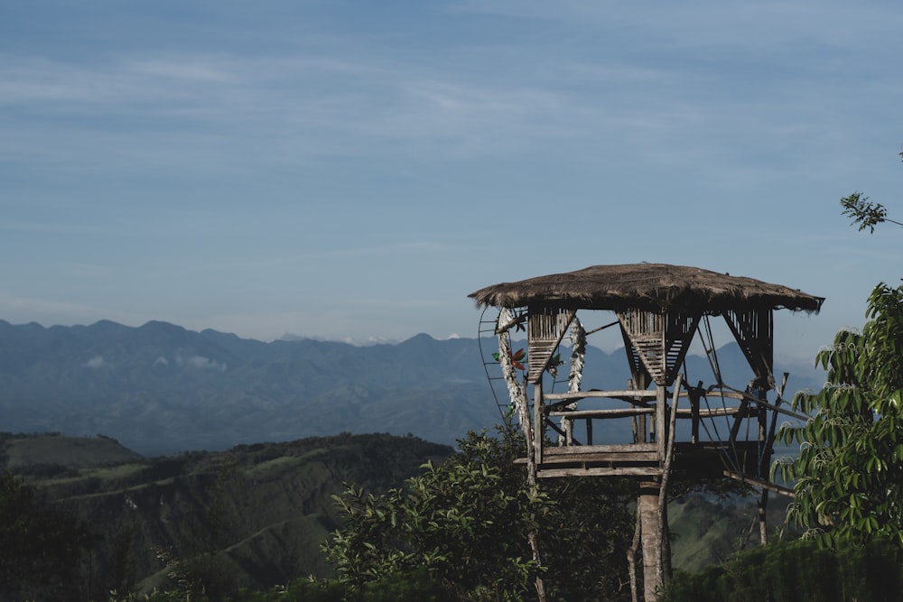 a wooden structure in the middle of a forest with mountains in the background
