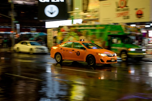 A yellow taxi car driving through busy Kuwait city streets at sunset