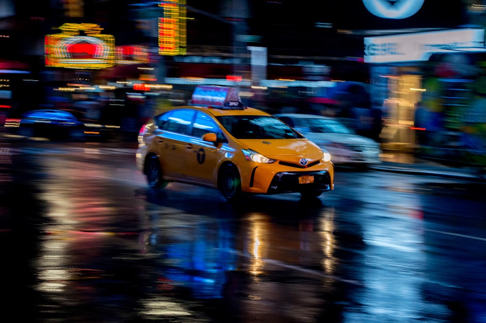 a yellow taxi cab driving down a rain soaked street
