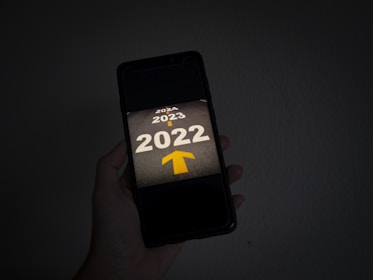 A hand holds a smartphone displaying the years 2022, 2023, and 2024 on a dark background, with a yellow arrow pointing forward from 2022 toward 2023 and 2024.