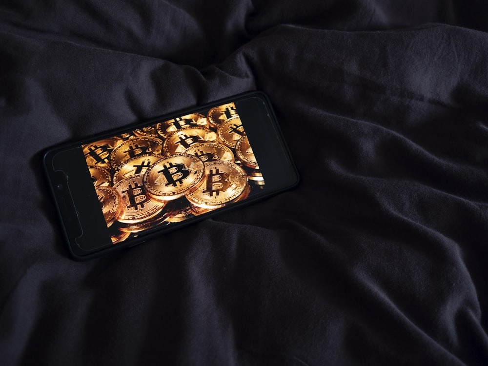 a cell phone sitting on top of a bed covered in gold coins