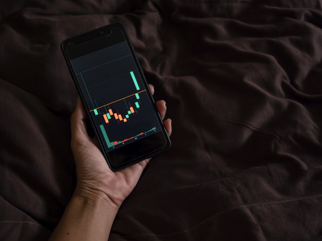 A hand holding a smartphone displaying a basic candlestick chart.