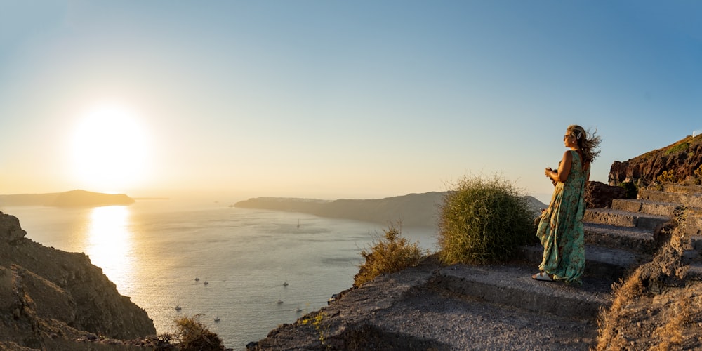 a woman standing on top of a cliff next to a body of water