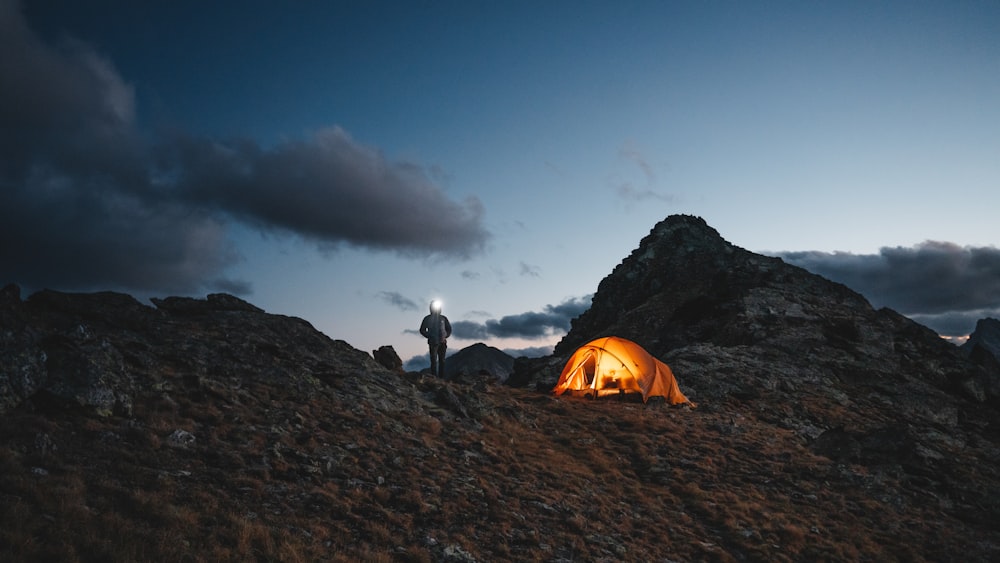 a man standing on top of a mountain next to a tent