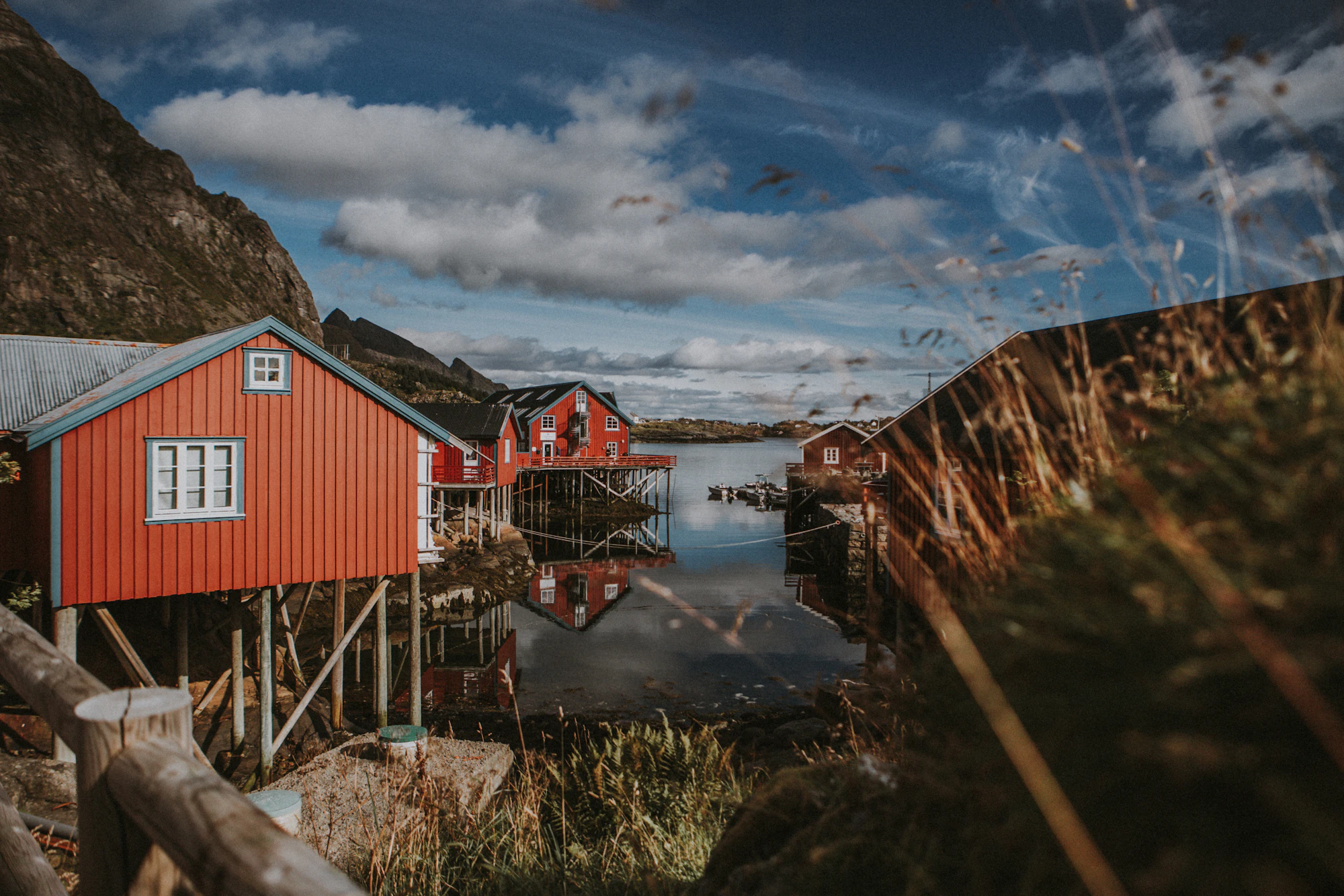 A red wooden house on stilts by the water, mountains behind