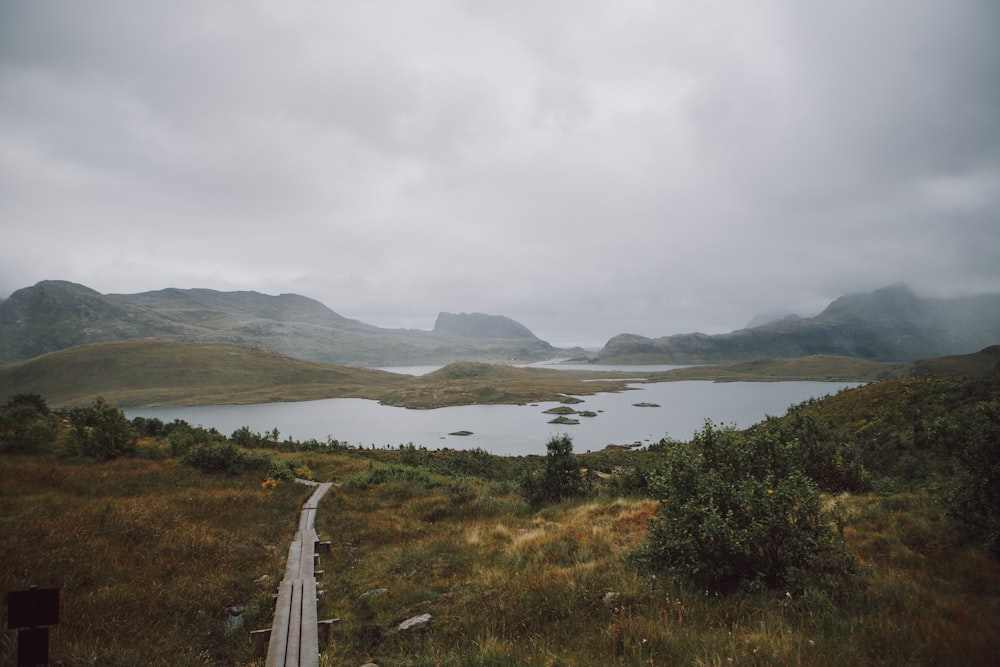 a wooden walkway leading to a lake surrounded by mountains