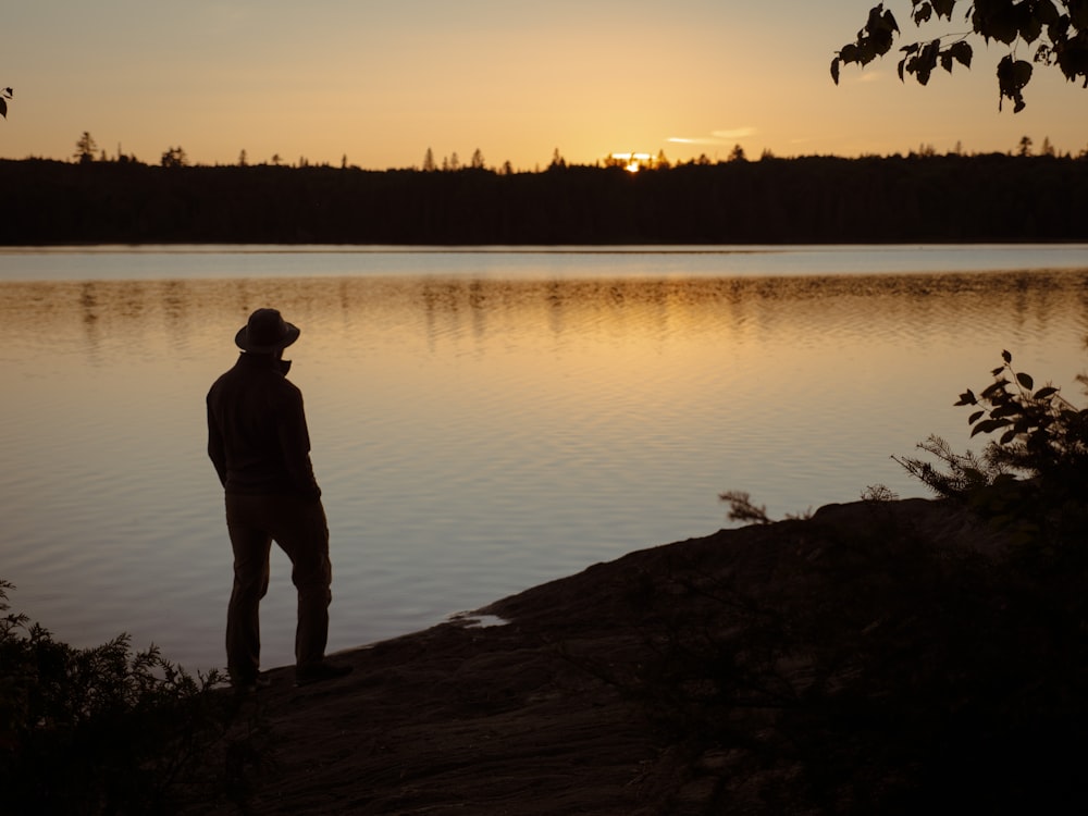 a man standing on the shore of a lake at sunset