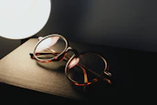Hands holding a sleek eyeglasses frame over an open book with soft natural lighting.