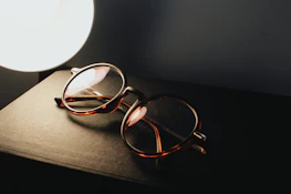 Hands holding a sleek eyeglasses frame over an open book with soft natural lighting.