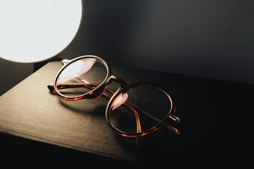 A close-up of stylish eyeglasses resting on an open book with soft natural light.