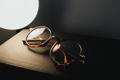 A stylish pair of classic eyeglasses placed on an open book with soft natural light.