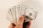 A hand holding a fan of hundred US dollar bills, displaying multiple notes in a splayed arrangement. The bills are crisp and new, showcasing the detailed design and printing.