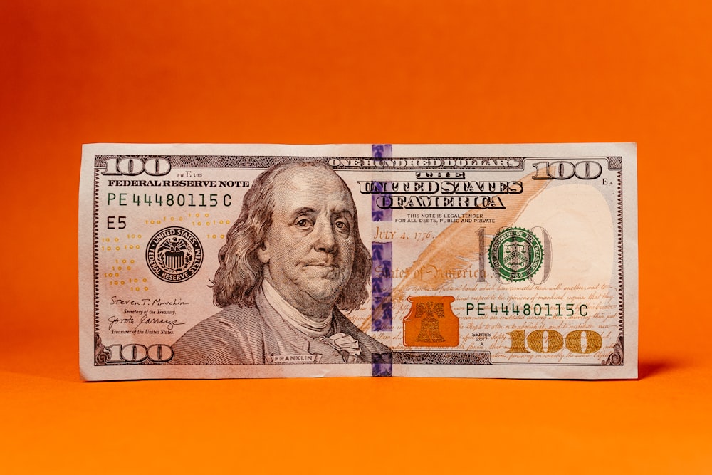 a one hundred dollar bill on an orange background