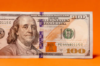 a one hundred dollar bill laying on top of an orange background