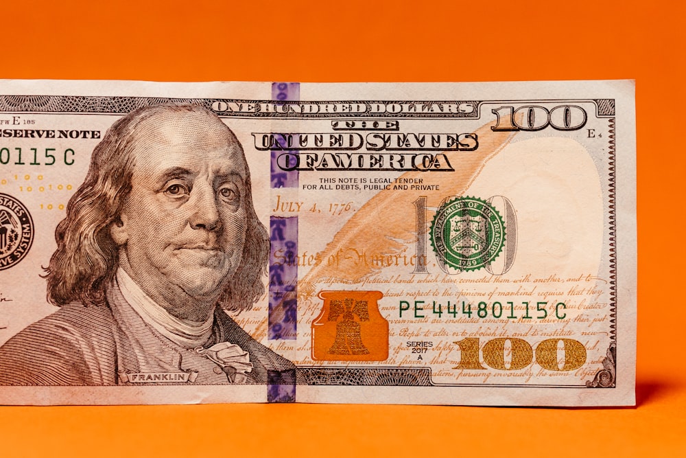 a one hundred dollar bill laying on top of an orange background