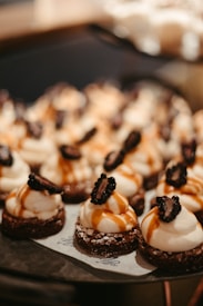 Creamy desserts topped with whipped cream and blackberries are neatly arranged on a plate. The desserts are drizzled with a golden caramel sauce, and each base is dusted with powdered sugar.