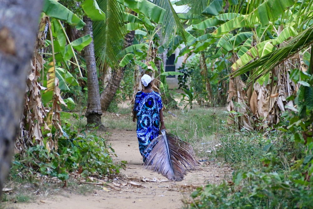 a woman walking down a dirt path with a peacock tail