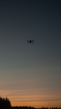A thermal drone hovering over a forest at dusk.