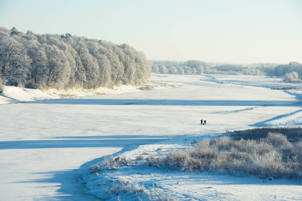 a couple of people walking across a snow covered field