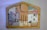 A wooden jigsaw puzzle with various painted sections. The sections depict abstract and somewhat childlike drawings of biblical figures and animals, including a person with a halo, another with a crown, and some animals that resemble sheep. The pieces fit into a house-shaped frame, each part forming a segment of the overall picture.
