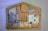 A wooden jigsaw puzzle with various painted sections. The sections depict abstract and somewhat childlike drawings of biblical figures and animals, including a person with a halo, another with a crown, and some animals that resemble sheep. The pieces fit into a house-shaped frame, each part forming a segment of the overall picture.
