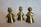 Three shiny brass figurines are displayed, each resembling a stylized, abstract human form. They have round heads and conical bodies, with one wearing a crown, indicating a royal theme. The surface of each figure reflects light with a yellowish tint.