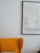 A cozy interior with a mustard yellow armchair partially visible next to a map of Copenhagen framed on a light-colored wall. The cushion and a pale flower bouquet add subtle detail to the scene.