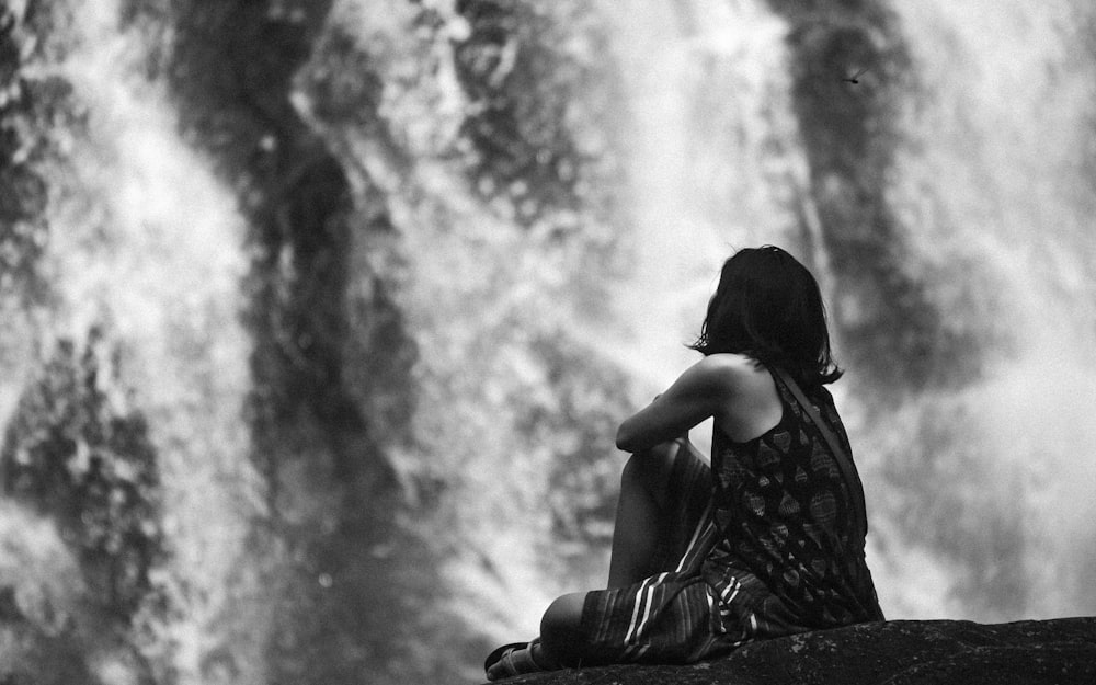 a woman sitting on a rock in front of a waterfall