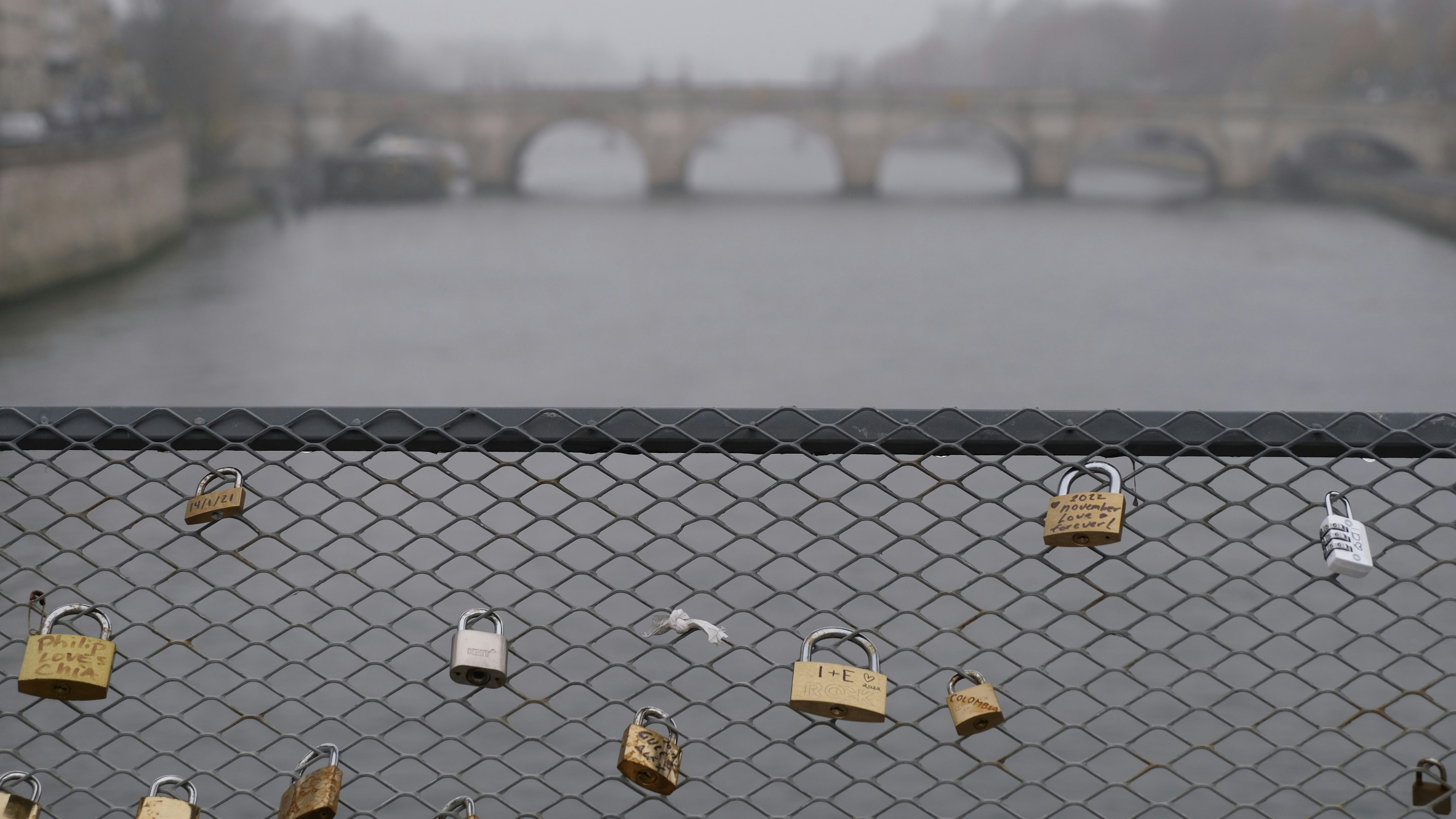 a fence with padlocks on it and a bridge in the background