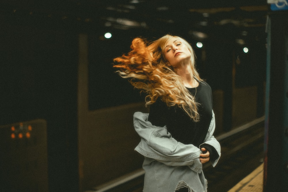 a woman standing on a train platform with her hair blowing in the wind