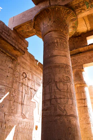 A detailed ancient Egyptian hieroglyphic carving on a temple wall under warm sunlight.