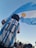 A person wearing a number 10 jersey with 'Messi' on the back stands in a crowd, holding a large Argentine flag against a clear blue sky.