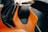A detailed view of a car seat with a luxurious design, featuring orange leather with black accents and an emblem on the headrest. The background is slightly blurred, indicating the interior of a high-end vehicle.