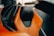 A detailed view of a car seat with a luxurious design, featuring orange leather with black accents and an emblem on the headrest. The background is slightly blurred, indicating the interior of a high-end vehicle.